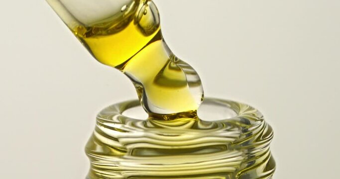 Serum or oil is dropped from a pipette with a dropper into a glass bottle. On a white background close-up.