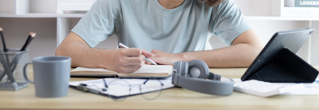 Asian man taking notes in notebook while studying online in tablet at home, Video chat, Online communication , Stay home, New normal, Distance learning., Social distancing, Learn online..