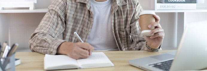 Asian man taking notes in notebook while studying online in laptop at home, Video chat, Online communication , Stay home, New normal, Distance learning, Social distancing, Learn online.