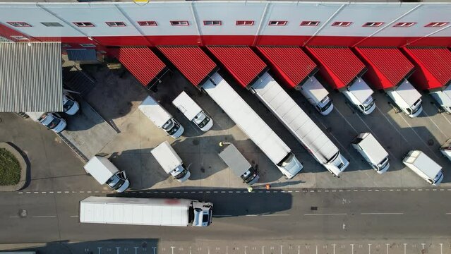Aerial top view of an industrial warehouse loading dock, where many delivery vans and trucks load goods. The logistics center and vehicles waiting to be loaded or unloaded.