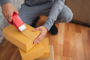Closeup of a young man packing parcels or cardboard boxes by using tape indoors for delivering product orders.Free space for text.