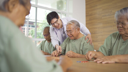 Fototapeta premium Portrait of happy group of old elderly Asian patient or pensioner people with a nurse and doctor playing games in nursing home. Senior lifestyle activity recreation. Retirement community. Health care