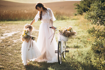 Mother with little daughter wearing beautiful dresses riding bicycle in the field