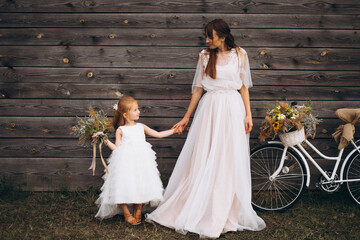Mother with little daughter wearing beautiful dresses riding bicycle in the field