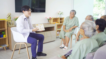 Obraz premium An Asian doctor talking to a group of old elderly patient or pensioner people smiling, relaxing, having fun together in nursing home. Senior lifestyle activity recreation. Retirement. Health care