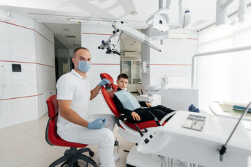 Fototapeta premium A young dentist examines and treats the teeth of an eight-year-old boy in modern white dentistry close-up. Dental prosthetics, treatment and teeth whitening. Modern dentistry. Prevention.