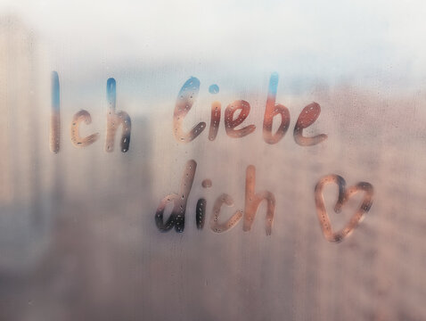 Lettering Deutsch text Ich liebe dich I love you in english and heart shape on sunset wet window