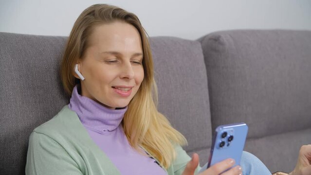 Cheerful blone woman listening to music online with a smartphone and wireless earphones