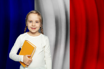 Happy child girl holding book in her hands on French flag background. Education and school in...
