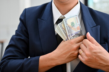 Close-up, A businessman putting a wad of US dollar bills into his suit pocket.