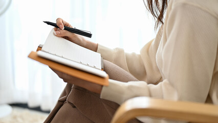 A female is writing her diary while sitting on her comfy armchair. cropped image