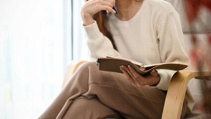 Pretty young Asian female reading a textbook in her modern minimal living room. cropped