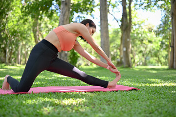 Fototapeta premium Sporty active Asian woman at park, stretching her arms and legs on yoga mat.