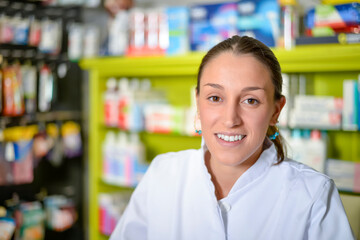 A Young pharmacist standing next to medicine shelves