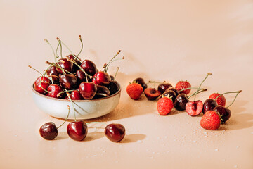 A large cherry with water drops close up in a gray deep plate on a light orange background in sunlight, selective focus. Front view