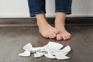 Barefoot woman standing near broken plate on floor, closeup
