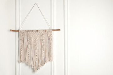 Stylish beige macrame hanging on white wall. Space for text