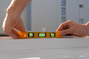 Worker using bubble level after plastic window installation indoors, closeup