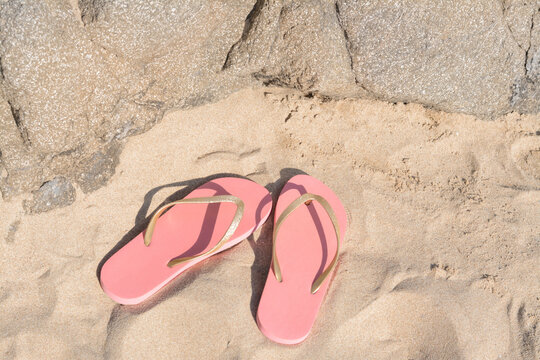 Stylish pink flip flops on sandy beach near rock, above view