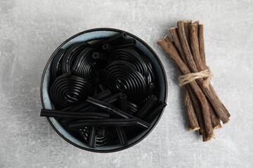 Tasty black candies and dried sticks of liquorice root on grey table, flat lay - Powered by Adobe