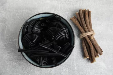 Tuinposter Tasty black candies and dried sticks of liquorice root on grey table, flat lay © New Africa