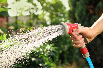Man spraying water from hose in garden, closeup - obrazy, fototapety, plakaty