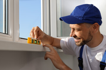 Worker using bubble level after plastic window installation indoors