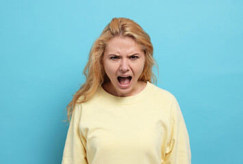 Aggressive young woman screaming with rage on light blue background - obrazy, fototapety, plakaty
