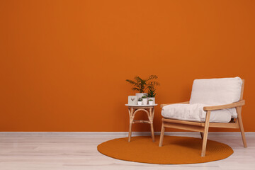 Stylish room interior with armchair and green plants near orange wall, space for text