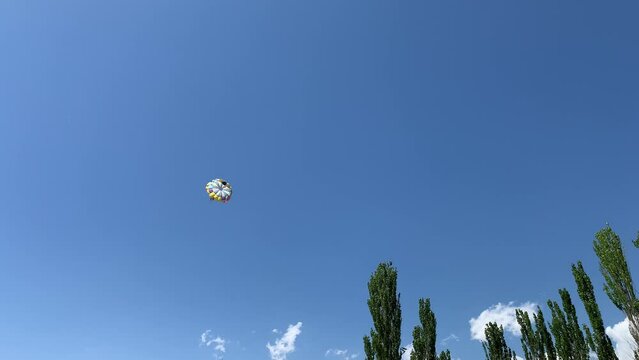A boat pulls a parachute across the sea with two tourists flying over the shore. Entertainment and active recreation of people at the sea in summer.