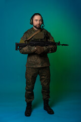 soldier in the studio on a green background with colored light. a man in military uniform with a gun, rifle or machine gun. military. airball player