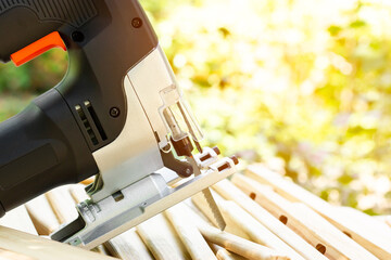 Electric jigsaw on wooden boards in sunlight. Power tool for woodworking. Carpentry work. Cutting a wooden board.
