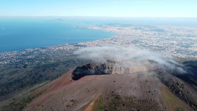 Aerial view of volcano Mount Vesuvius, rough volcanic terrain inside crater on top of mountain - panorama of Naples from above, Italy, Europe. Epic reveal. Drone footage 4K. Cloud over volcano.