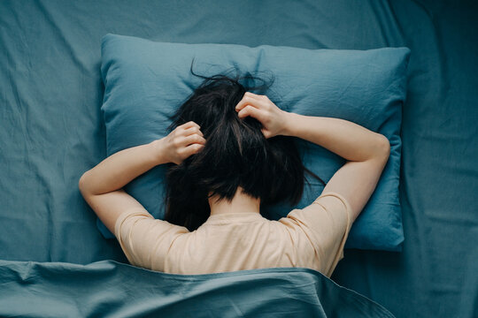 The young woman in bed hugged her head. Depression or mental health problems. Top view.