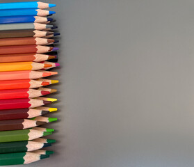 On a metal, gray table there are two rows of colorful drawing pencils. The pencils are well sharpened. A great set for an artist