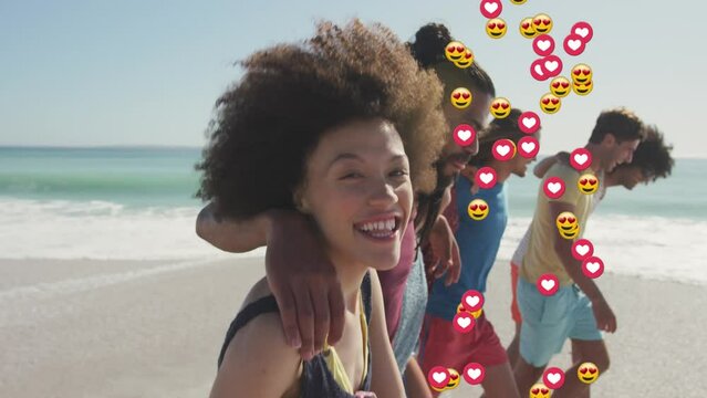 Animation of hearts and love emojis over diverse group of happy friends walking on sunny beach