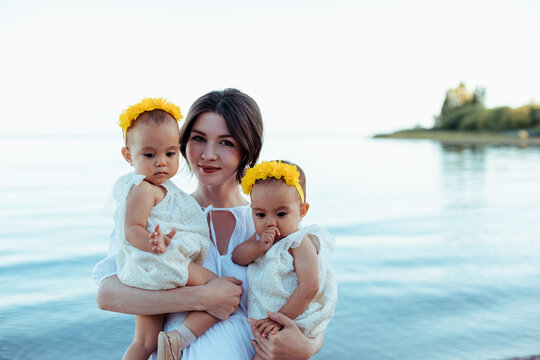 Mother Holding Twin Daughters On The Beach All In White Clothes