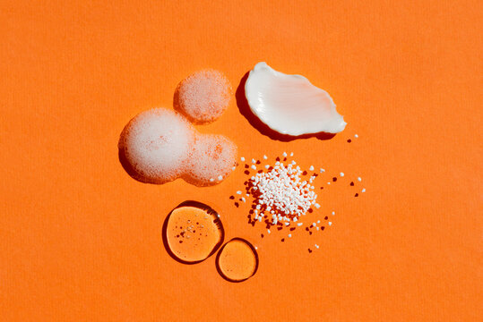 Close up cosmetic swatch and drops. Appearance of the texture of the cream, gel, foam and granules on a orange background. Natural skincare products. Beauty concept for face and body care