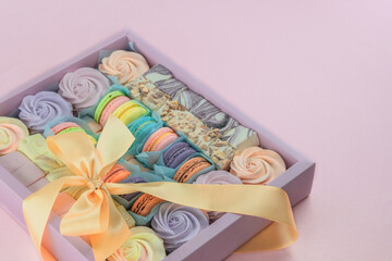 Macaroons and marshmallows in box in pink background, closeup. Traditional colored sweet desserts for present for the holiday.