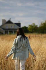 a girl walks across a field with dry grass in a shirt towards a house in the distance