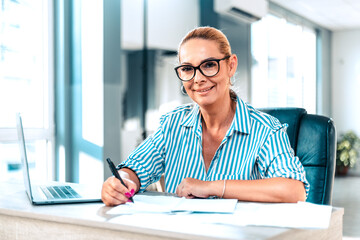 Confident european mature middle aged woman sitting at office. Stylish businesswoman, 40s lady executive leader manager looking at camera in office, portrait..