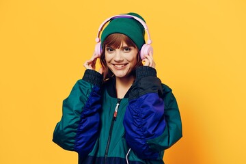horizontal photo of a beautiful woman in a jacket and hat listening to music with pink headphones holding them with her hands