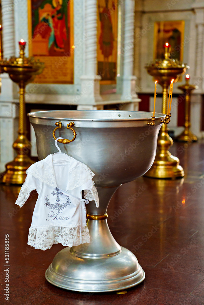 Sticker a baptismal shirt hangs on the baptismal font in the church.