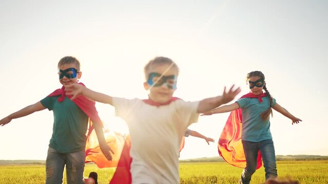 team of kids superheroes run. happy family kid concept. a group of children playing superheroes in capes and masks run through the grass at sunset. success business striving dream for goal concept