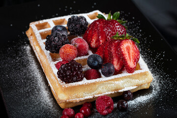 Traditional Belgian waffles with ice cream and berry fruit sauce on plate, selective focus and free space. Macro shot of waffles with, blueberries , blackberries and caramel.