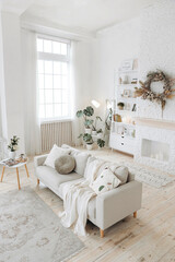 Modern stylish white living room with large windows and scandinavian style sofa against the backdrop of a fireplace and shelving and potted plants. Nobody