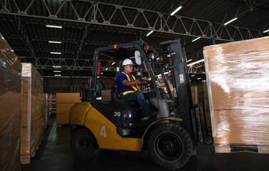Warehouse worker driver in uniform delivery and loading pallet product by forklift.