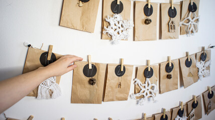 Female hand snaps off a wooden clothespin with the 17th day in the advent calendar. Eco-friendly zero waste advent calendar with craft bags and macrame, wooden figurines on the wall. Eco Christmas
