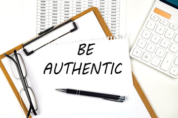 Text BE AUTHENTIC on the white paper on clipboard with chart and calculator