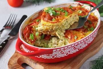 Homemade zucchini casserole with chicken, tomatoes and cheese in a ceramic mold on wooden board, Close-up